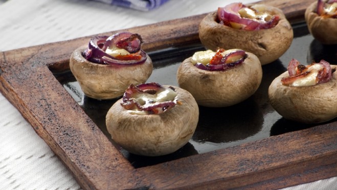 Imagem de cogumelos recheados com queijo e tomate seco sobre uma tábua de madeira