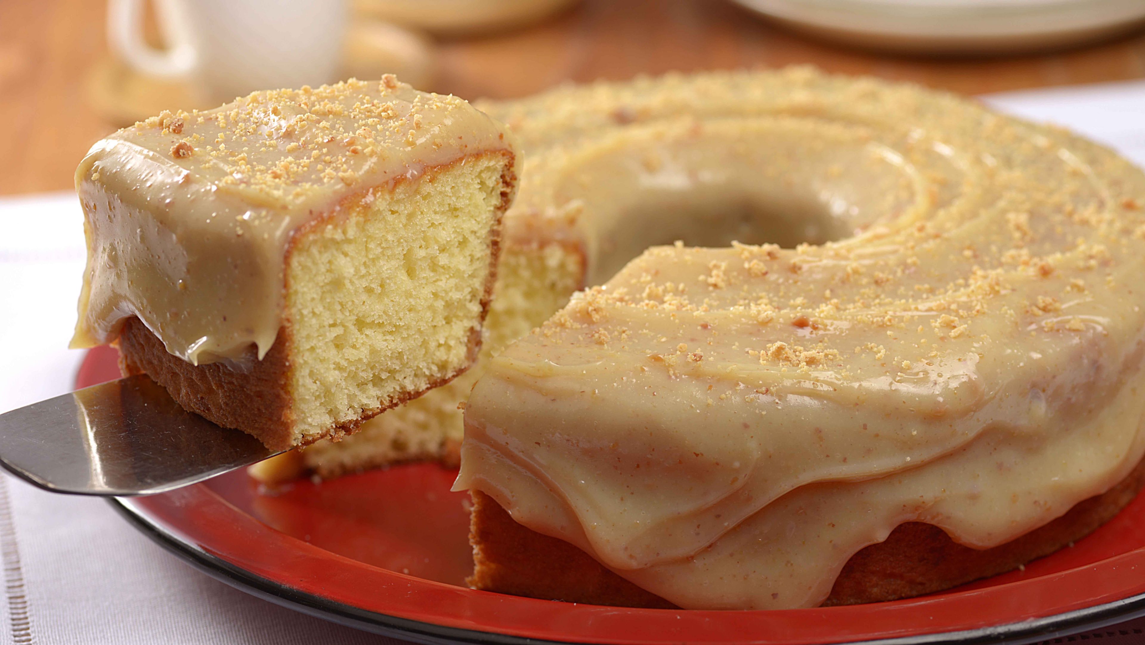 Imagem de um bolo de queijo com cobertura de paçoca, sendo cortado